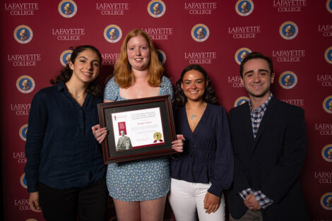 Four students smile with an award.
