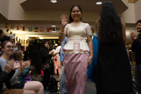 A student waves as they walk down a catwalk, modeling an outfit during a fashion show.