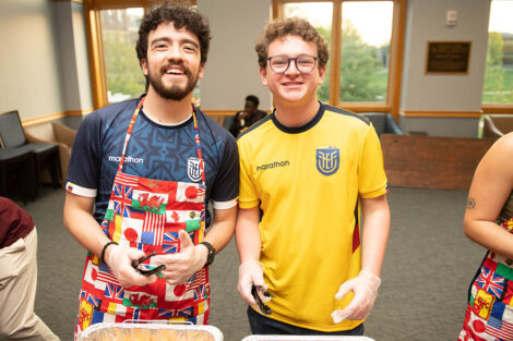 Two students smile, serving food.