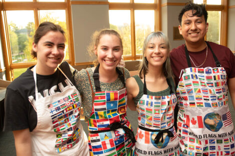 Students wearing aprons with international flags on it smile.