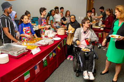 Lines of students serve international cuisine to other students, as Nicole Hurd speaks to a student.