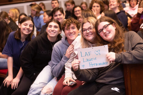 A crowd of students smile; one holds a sign that reads: Laf loves Laurie Hernandez.
