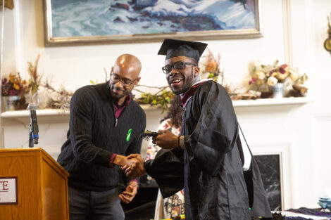 A staff member shakes hands with a student, wearing a cap and gown.