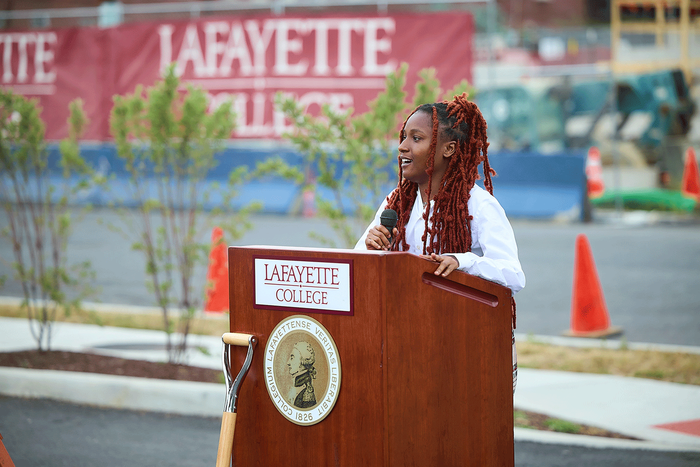 Jada Peters '24 speaks at a podium during a groundbreaking. She is holding a microphone.