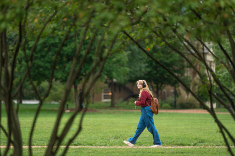 A student walks across the grassy Quad.