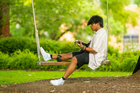 A student plays the guitar on a swing.