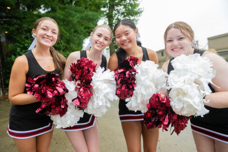 Cheerleaders smile, holding pom poms.
