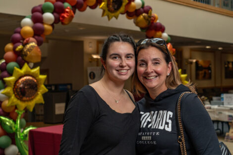 Two women stand in front of a balloon arch. One woman is wearing a Leopards sweatshirt.