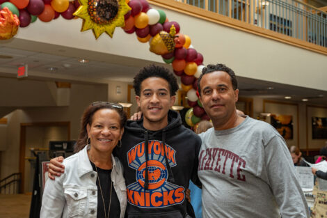 A student is standing in between his parents in front of a balloon arch.