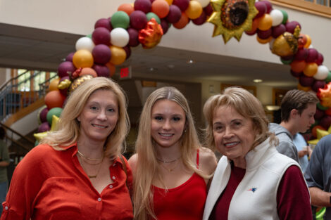 Three women stand in front of a balloon arch. They are wearing red and white.