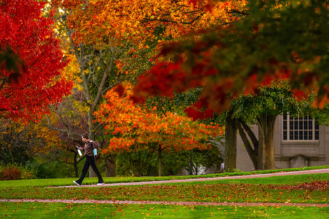 A student adjusts their backpack while walking on a campus path.