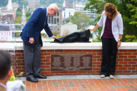 Audra Kahr and an alum lift the cover off the plaque of named supporters during the The Class of 1962 Gateway Plaza Dedication Sept. 28