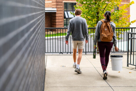 Katie Liu '25 and Pierson White '24 walk away from the camera; Katie carries a reusable water bottle and a bucket of compost.
