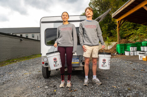 Katie Liu '25 and Pierson White '24 smile while holding buckets in front of an electric vehicle.