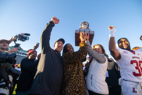 Coach Troxell, Sherryta Freeman, Nicole Hurd, and football players raise the trophy.