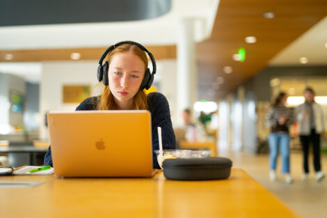 A student studies on their laptop in Rockwell. The student wears headphones.