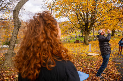 A student watches David Sunderlin speak, surrounded by fall trees.