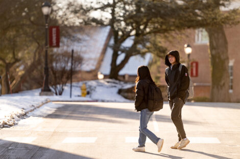 Two students talk and cross the street on campus.