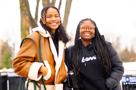 Two smiling students are photographed in front of the Quad.