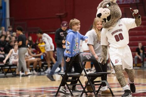 Two students play musical chairs with the Leopard mascot.