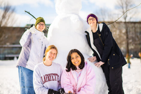 A group photo of students in front of a snowman.