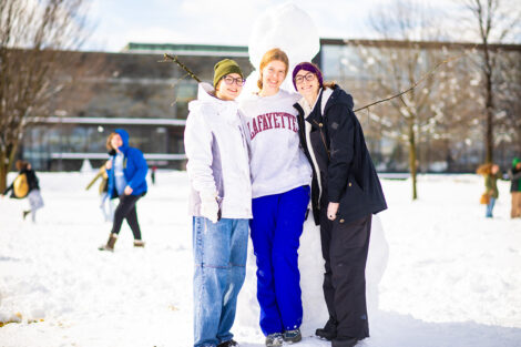 A group photo of students in front of a snowman.