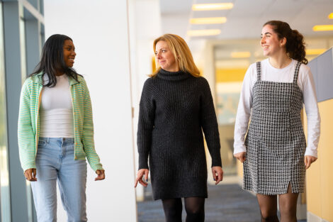 Krista Ortwein ’05 walks down a hallway and chats with Elle Lansing ’26 and Charlize Cramer ’24