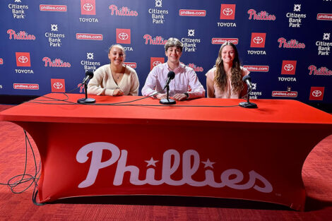 Courtney Campbell ’25, Jeremy Frankel ’24, and Anna Gonella ’25 sit at a Phillies press table in front of the Phillies logo