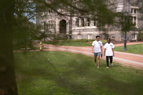 Two student walk together along a campus pathway towards the Quad.