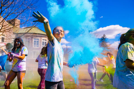 A student throws blue powder into the air at the Holi Fest.