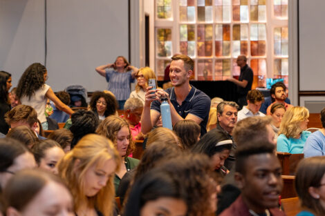 A professor stands and takes a photo on his cell phone in a crowd of Colton.