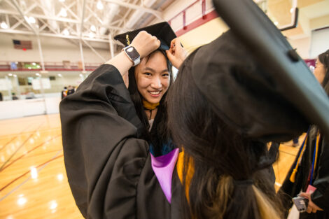 A student has help putting on their graduation cap.