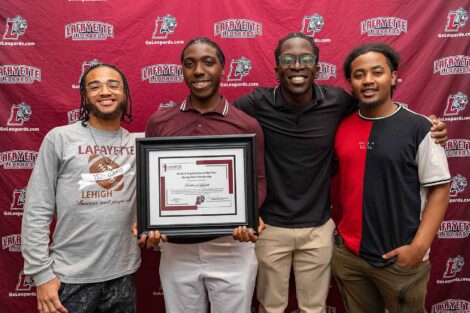 Four students stand smiling against a Lafayette Leopards backdrop. One student is holding a framed award.