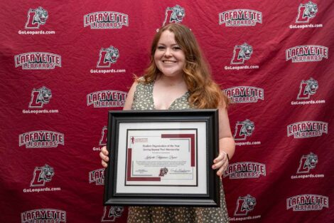 Devin is standing in front of a Lafayette Leopards backdrop holding a framed award.