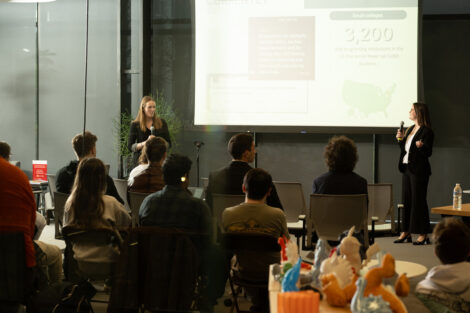 Two students present their ideas on a large screen.