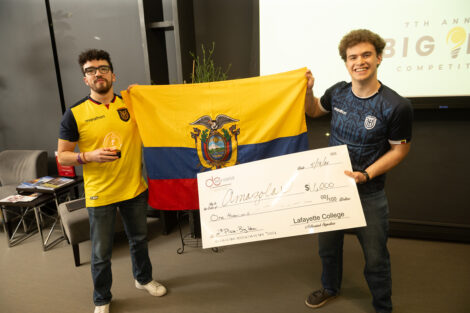 Two students hold a flag and a large check for second place.