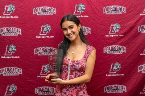 Emma is standing against a Lafayette Leopards backdrop and holding a glass award.