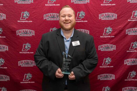 Jake is standing against a Lafayette Leopards backdrop and holding an award.