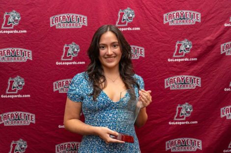 A student is standing against a Lafayette Leopards backdrop holding an award. She is wearing a blue dress.