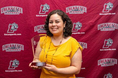 Karina Fuentes is holding a glass award and standing against a Lafayette Leopards backdrop.