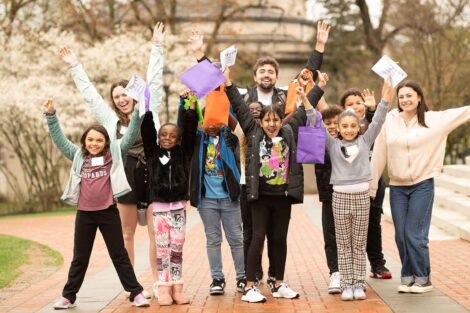 A group of EASD elementary school students pose and wave their hands in the air with their college pen pals on the Quad.