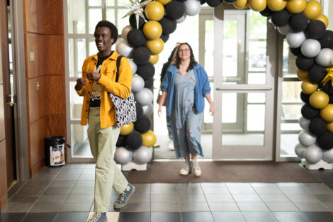 Students walk through a black, white, and gold ballon arch.