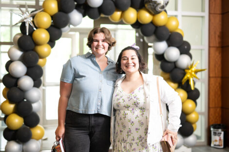 Students smile in front of a black, white, and gold ballon arch.
