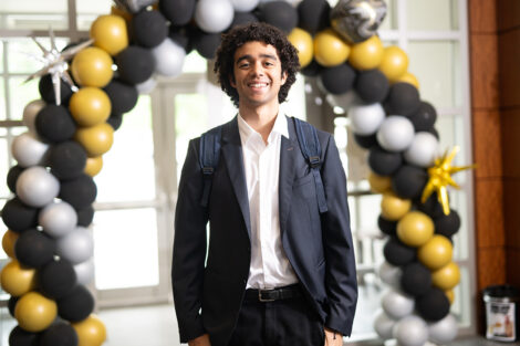 A student walks through a black, white, and gold ballon arch.