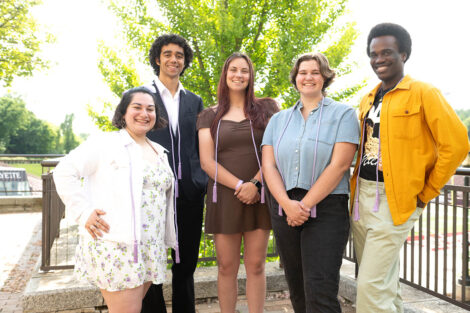 Five students smile, wearing lavender cords.