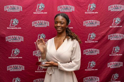 Natalie is standing against a Lafayette Leopards backdrop and holding a glass award.