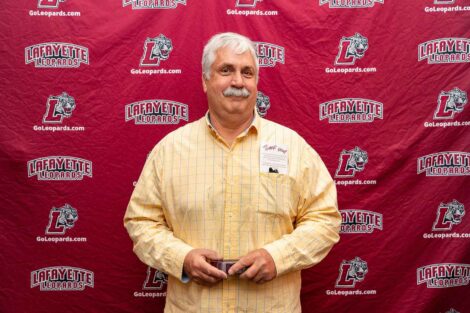 Ray is standing against a Lafayette Leopards backdrop and holding a wooden award.