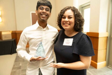 Sidharth Mahadeo ’26 and Karina Fuentes are standing next to each other and smiling. Sidharth is holding a glass award.