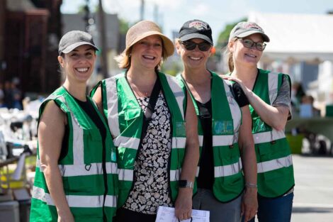 Four Lafayette volunteers in hats and green vests smile during the West Ward Sale.