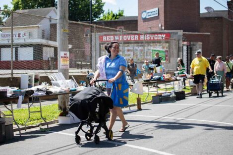 A woman pushes a baby stroller past items available during the West Ward Sale.